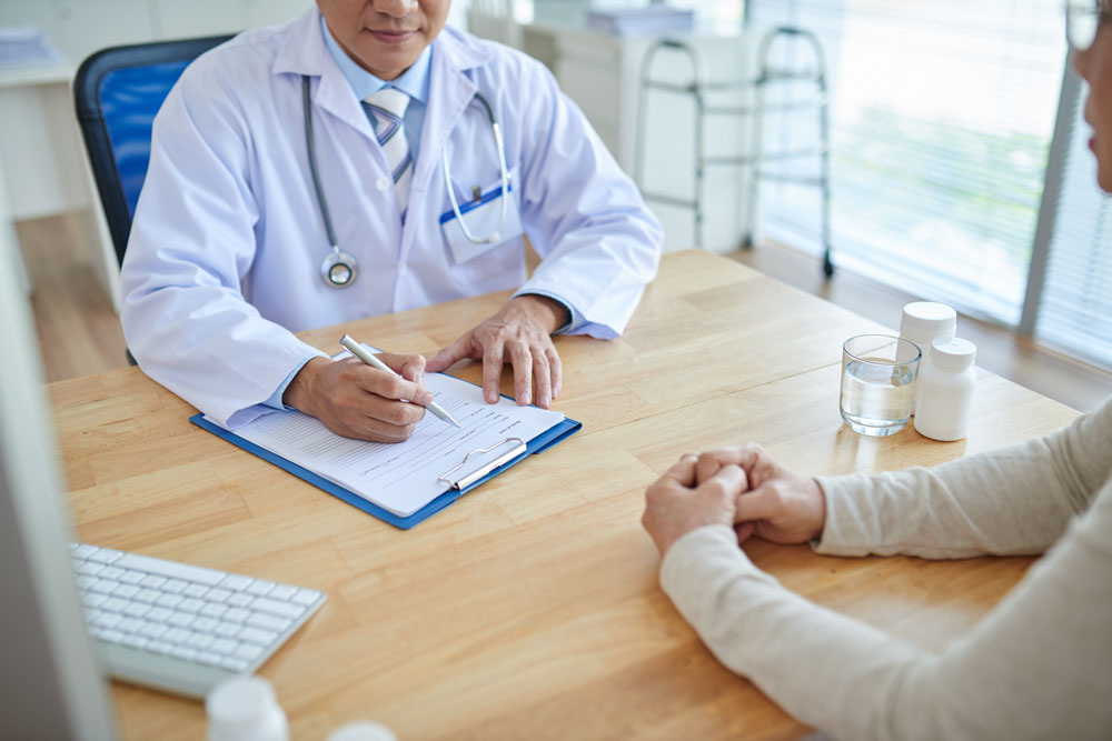 Médico llenando una Historia clínica mientras habla con su paciente